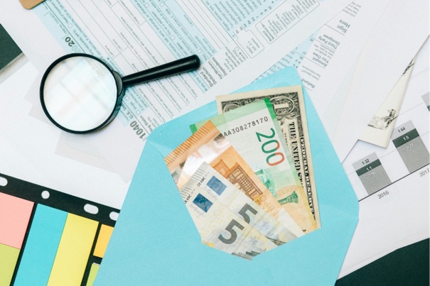 Envelop met eurobiljetten en dollars op belastingformulieren met een vergrootglas